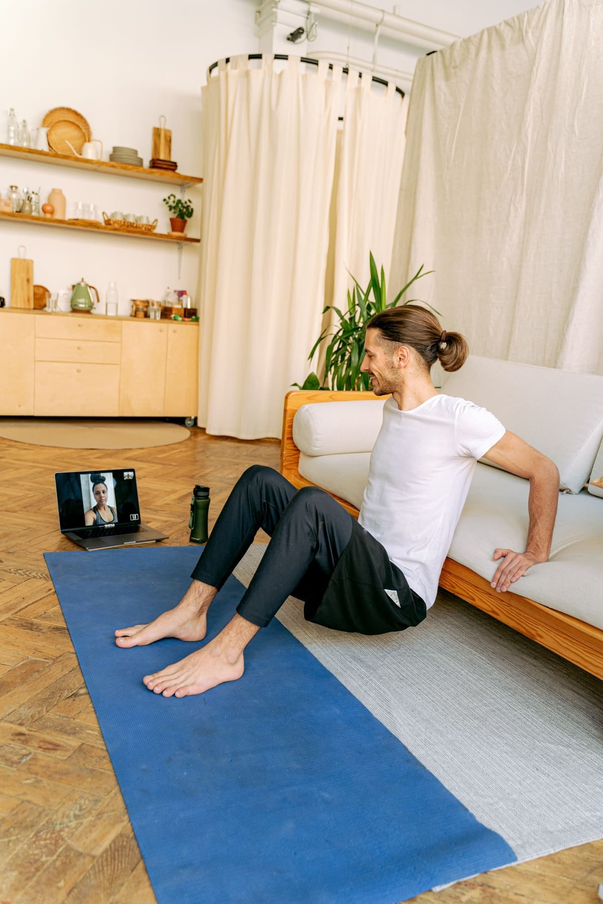 A man following a physiotherapist's guidance on a laptop video call from his living-room floor